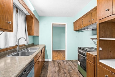 Kitchen with dark wood finished floors, electric stove, under cabinet range hood, stainless steel dishwasher, and brown cabinetry