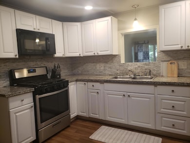 kitchen with stainless steel gas range oven, white cabinetry, black microwave, and tasteful backsplash