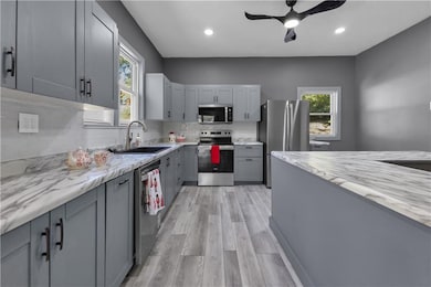 Kitchen featuring stainless steel appliances, light wood-type flooring, decorative backsplash, gray cabinets, and plenty of natural light