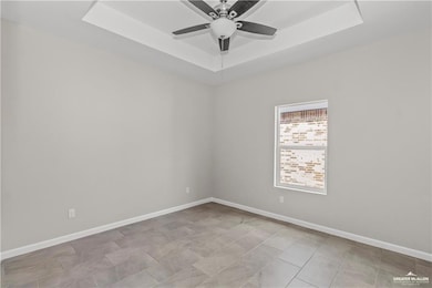 Empty room featuring baseboards, a ceiling fan, and a raised ceiling
