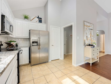 Kitchen featuring black range with electric cooktop, high vaulted ceiling, arched walkways, stainless steel fridge, and white​​‌​​​​‌​​‌‌​​‌​​​‌‌​​​​​​‌‌‌​​‌​​‌‌​​​‌ cabinetry