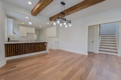 Unfurnished living room with light wood-style flooring, recessed lighting, stairs, a sink, and beamed ceiling