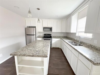 Kitchen with open shelves, appliances with stainless steel finishes, a center island, pendant lighting, and light stone countertops