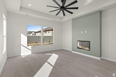 Unfurnished living room featuring carpet floors, a glass covered fireplace, ceiling fan, a raised ceiling, and recessed lighting