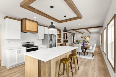 Kitchen with white cabinets, appliances with stainless steel finishes, a center island, and light wood-type flooring