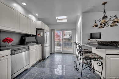 Kitchen featuring white cabinets, stainless steel appliances, hanging light fixtures, stainless steel countertops, and a skylight