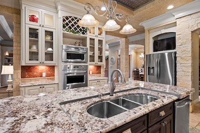 Kitchen featuring ornate columns, crown molding, stainless steel appliances, tasteful backsplash, and light stone countertops