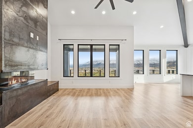 Unfurnished living room with a multi sided fireplace, light wood-style floors, recessed lighting, a mountain view, and ceiling fan