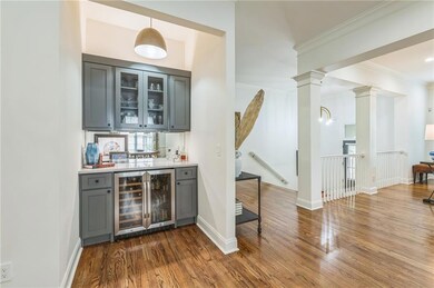 Indoor dry bar with wine cooler, dark wood finished floors, ornate columns, crown molding, and baseboards. Cozy up for a cocktail! This bar was installed in what can also be retrofitted for an elevator. Shaft runs to all 3 floors!