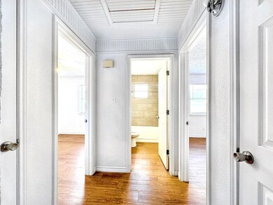 Hall with baseboards, attic access, and wood fini
