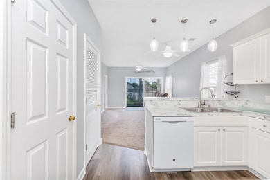 Kitchen with dishwasher, a sink, a ceiling fan, open floor plan, and white cabinets