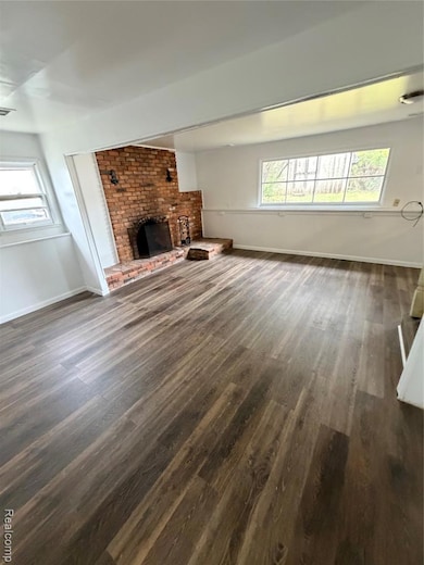 Unfurnished living room featuring a brick fireplace and dark wood-type flooring
