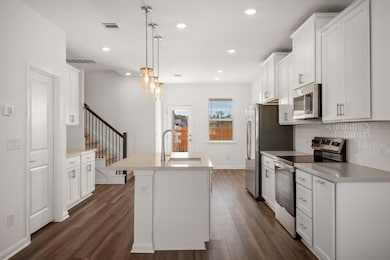 Kitchen with sink, stainless steel appliances, white cabinets, a center island with sink, and decorative light fixtures