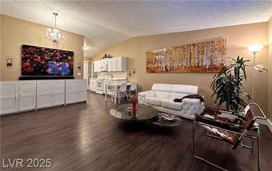 Living room with a chandelier, dark wood finished floors, a textured ceiling, and vaulted ceiling
