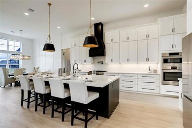 Kitchen with white cabinets, light countertops, an island with sink, and custom exhaust hood