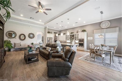 Living room with light wood finished floors, recessed lighting, ceiling fan, arched walkways, and ornamental molding