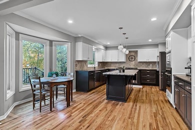 Kitchen with ornamental molding, decorative light fixtures, dark stone countertops, light wood-style floors, and white cabinetry