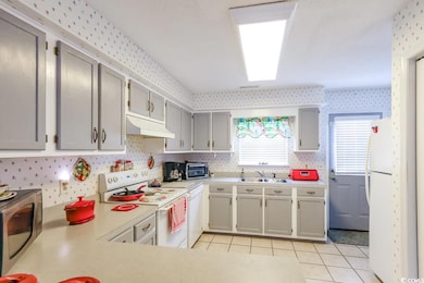Kitchen with under cabinet range hood, white appliances, a sink, wallpapered walls, and light countertops