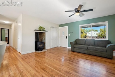 Living area featuring a wood stove, light wood-style flooring, and a ceiling fan