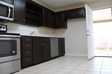Kitchen featuring appliances with stainless steel finishes, dark brown cabinetry, open shelves, and light tile patterned floors