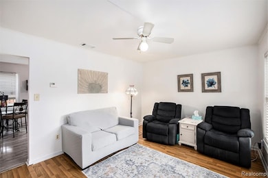 Living area featuring plenty of natural light, wood finished floors, a ceiling fan, and crown molding