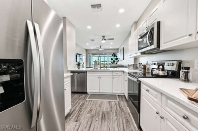 Kitchen with stainless steel appliances, white cabinetry, light wood-style flooring, recessed lighting, and light stone countertops