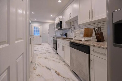Kitchen with white cabinets, stainless steel appliances, light stone counters, tasteful backsplash, and light marble finish floors