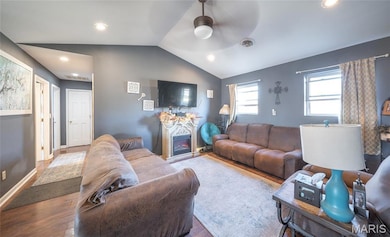 Living area featuring vaulted ceiling, wood finished floors, a warm lit fireplace, ceiling fan, and recessed lighting