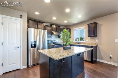Kitchen with stainless steel appliances, under cabinet range hood, dark brown cabinets, light stone counters, and baseboards
