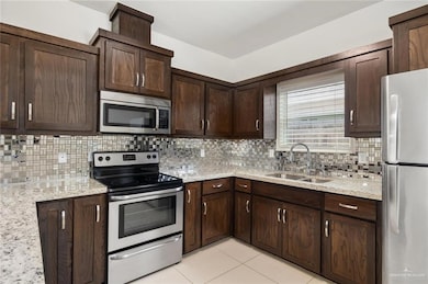 Kitchen with appliances with stainless steel finishes, dark brown cabinetry, light tile patterned floors, and backsplash