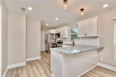 Images are of a model home and may include custom design features not available in other homes. Kitchen with light stone countertops, white cabinets, a peninsula, light wood-style flooring, and recessed lighting
