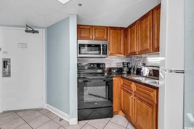Kitchen featuring black electric range oven, dark stone counters, stainless steel microwave, brown cabinets, and light tile patterned flooring