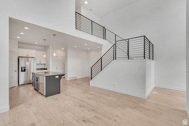 Kitchen with a towering ceiling, light wood-style flooring, a center island with sink, recessed lighting, and stainless steel fridge with ice dispenser