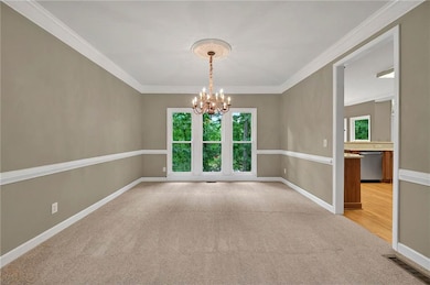 Dining room room with a chandelier, light colored carpet, baseboards, and ornamental molding