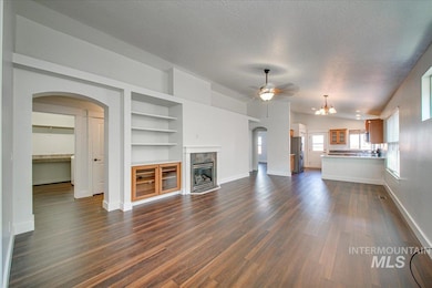 Unfurnished living room featuring arched walkways, a high end fireplace, a textured ceiling, a ceiling fan, and built in shelves