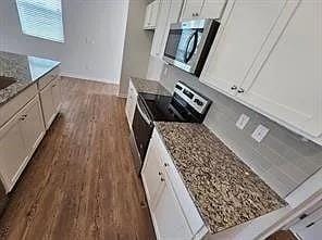 Kitchen featuring dark wood-style flooring, stainless steel appliances, white cabinetry, and light stone counters