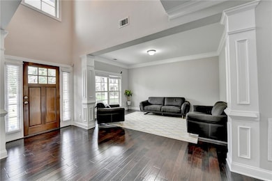 Foyer entrance with decorative columns, dark wood finished floors, crown molding, baseboards, and a towering ceiling