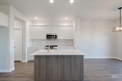 Kitchen featuring stainless steel appliances, backsplash, a center island with sink, white cabinetry, and hanging light fixtures