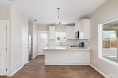 Kitchen with appliances with stainless steel finishes, decorative backsplash, white cabinets, a chandelier, and wood finished floors