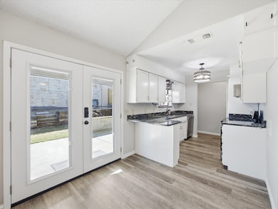 Kitchen with white cabinetry, a peninsula, french doors, light wood-style flooring, and dark stone counters