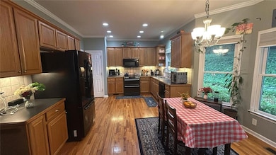 Kitchen featuring black appliances, a chandelier, open shelves, light wood-style flooring, and dark countertops