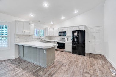 Kitchen with decorative backsplash, lofted ceiling, black appliances, a peninsula, and light wood-type flooring