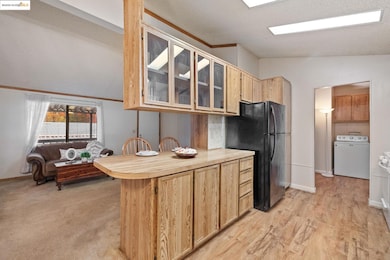 Kitchen with light brown cabinets, lofted ceiling, glass insert cabinets, washer / clothes dryer, and freestanding refrigerator