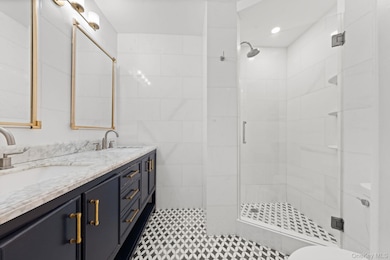 Bathroom featuring a stall shower, double vanity, and tile walls