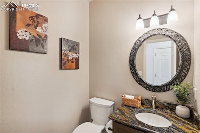 Half bath with toilet, vanity, and a textured wall