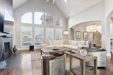 Living room with high vaulted ceiling, a fireplace with flush hearth, arched walkways, dark wood finished floors, and a ceiling fan