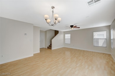 Empty room with a chandelier, light wood-style floors, a ceiling fan, and stairs