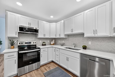 Kitchen featuring stainless steel appliances, white cabinets, light wood-style floors, tasteful backsplash, and recessed lighting