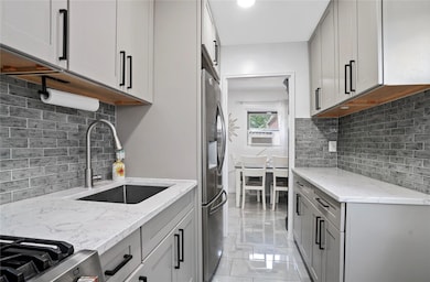 Kitchen with gray cabinetry, tasteful backsplash, light stone counters, stainless steel fridge with ice dispenser, and light marble finish floors