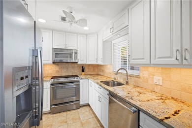 Kitchen featuring appliances with stainless steel finishes, light stone counters, white cabinetry, backsplash, and recessed lighting